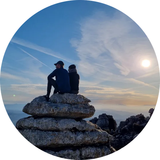 Chris and Shadi sitting back-to-back on a rock formation at sunset